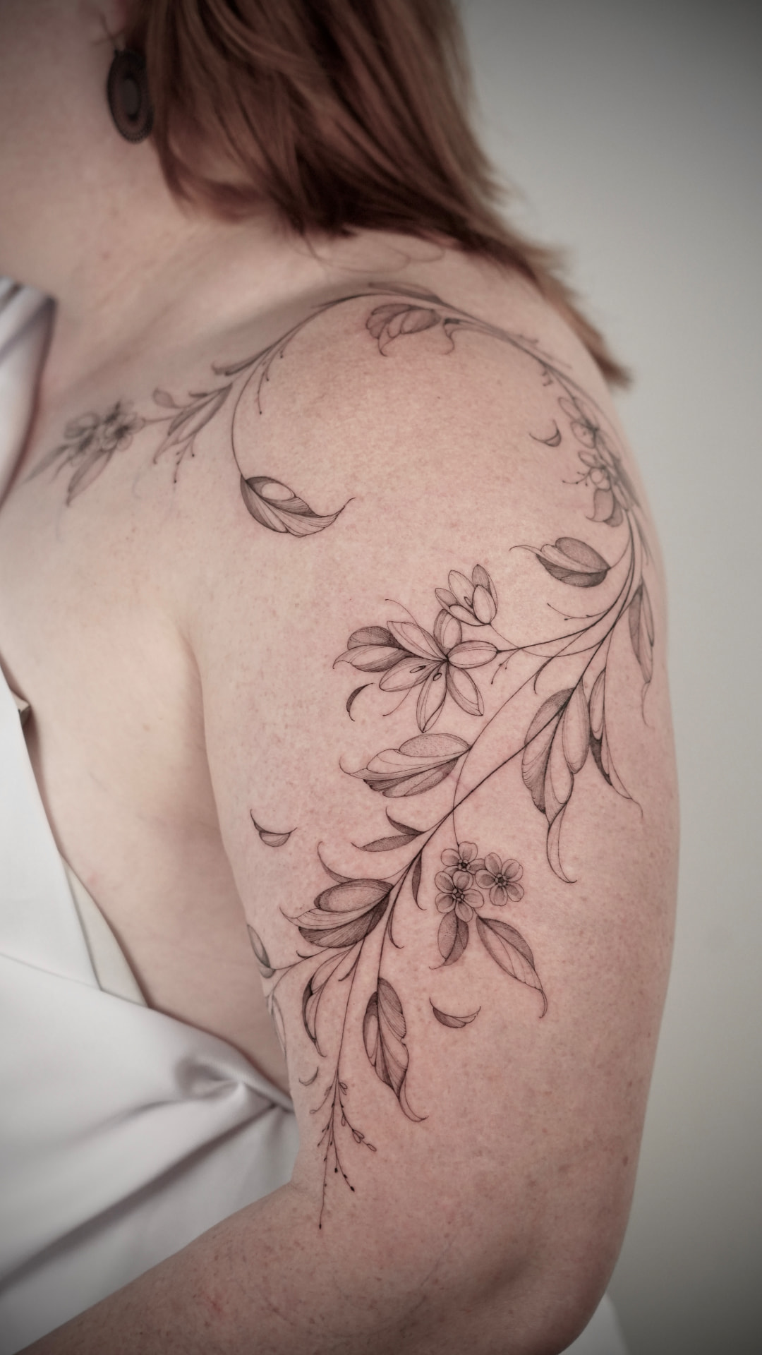 Fine line botanical tattoo of flowering branches wrapping the shoulder and upper arm, tattooed at London's Glitch