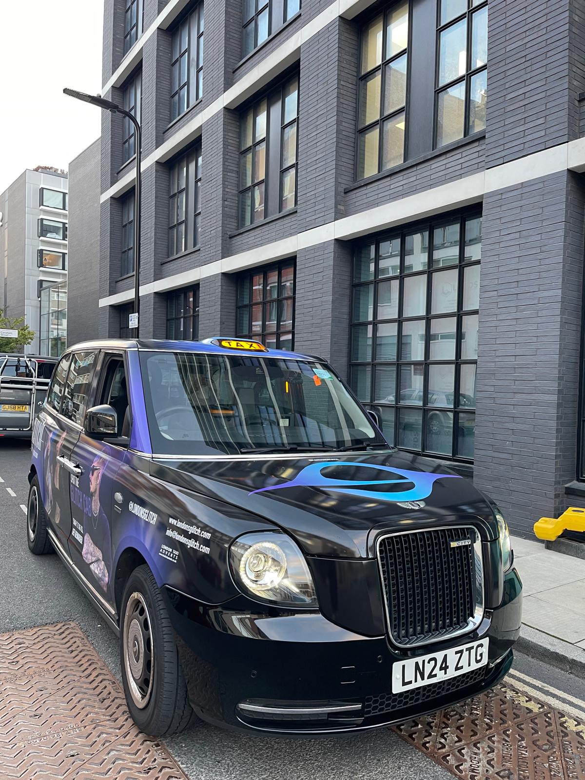Front three-quarter view of the branded London's Glitch black cab with the blue Glitch eye on the bonnet