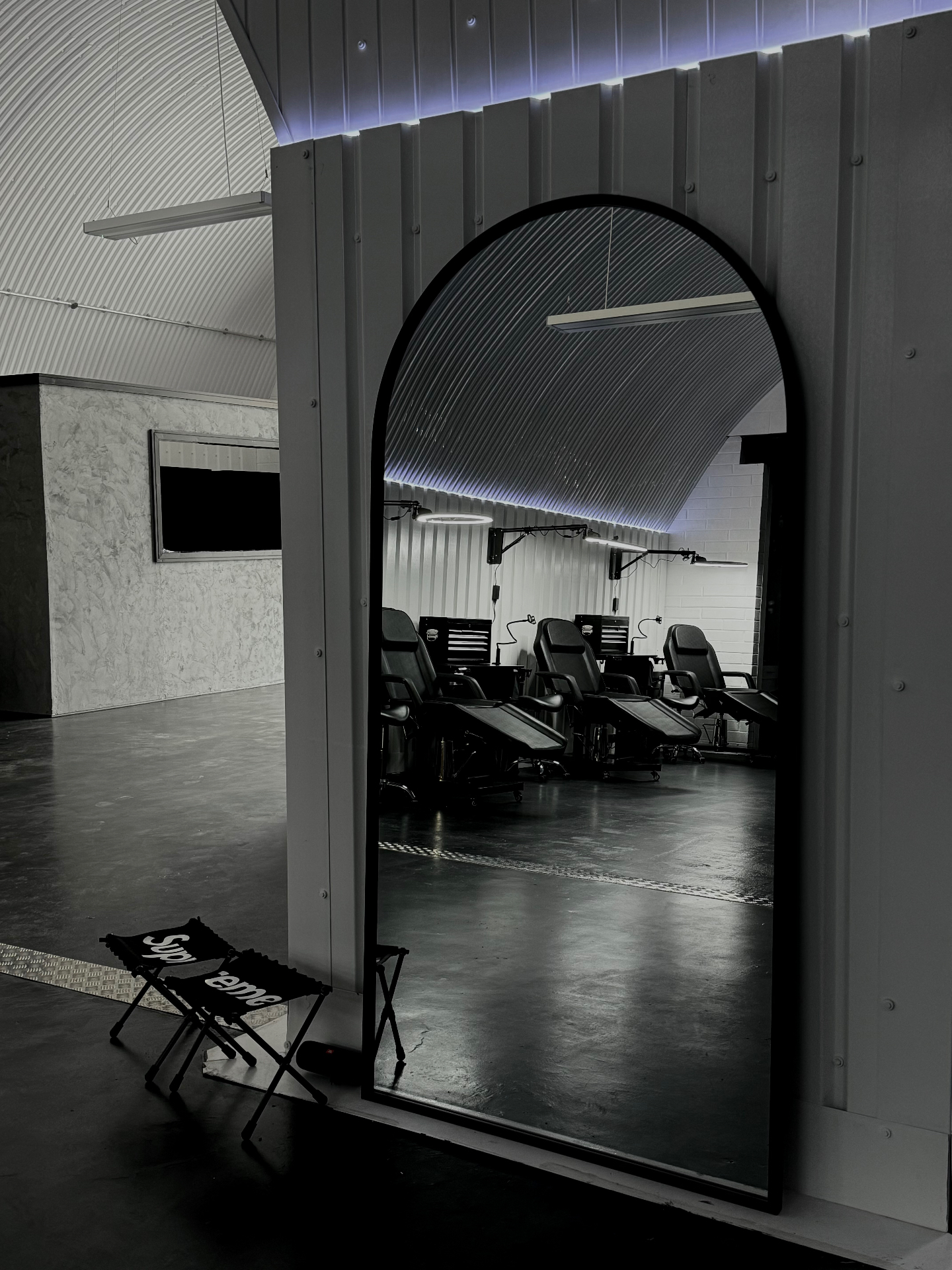 Full-length mirror reflecting the row of tattoo stations across the glossy black floor