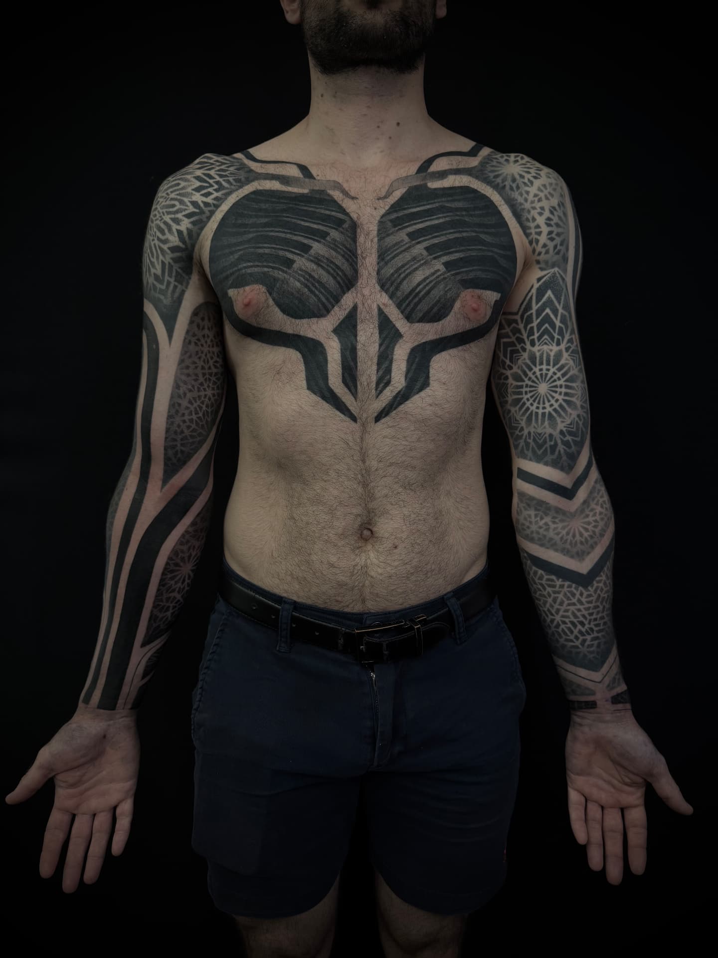 Large-scale dotwork and geometric blackwork tattoo across the chest and both arms, tattooed at London's Glitch