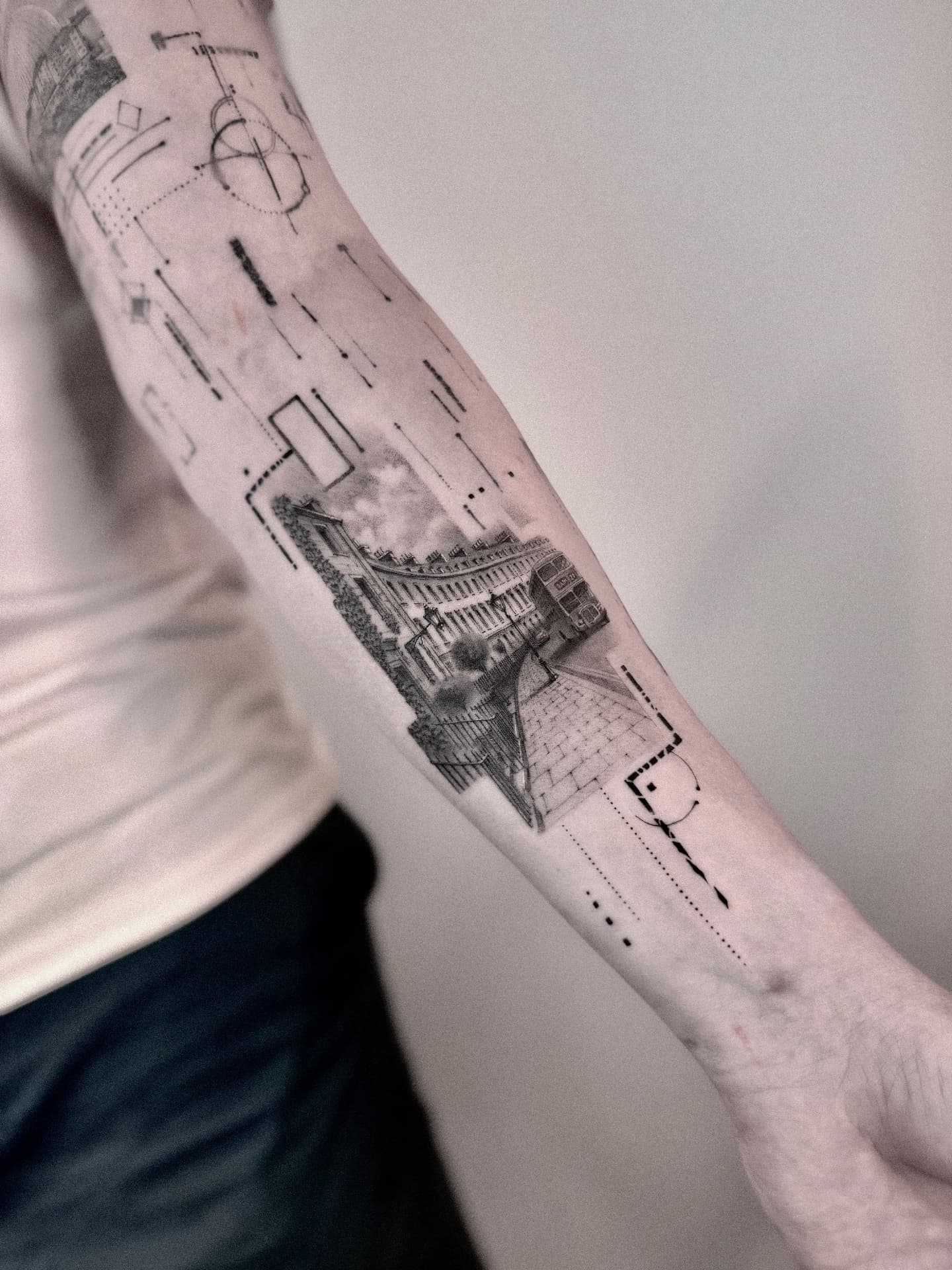 Microrealism tattoo of a curved architectural street scene with a double-decker bus, framed by fine-line geometric and blueprint-style elements, running down the inner forearm, tattooed at London's Glitch