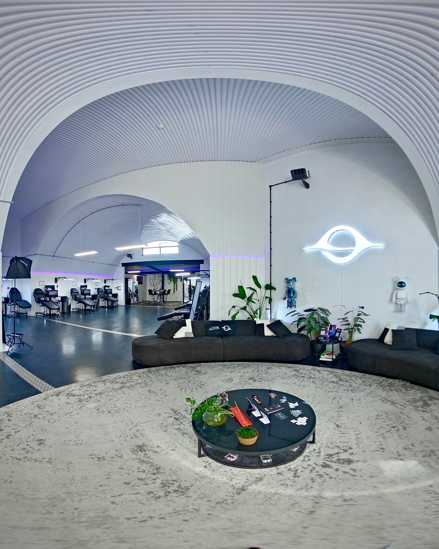 The lounge at London's Glitch — black sofas, round rug and the illuminated white Glitch eye on the wall beneath the railway arch