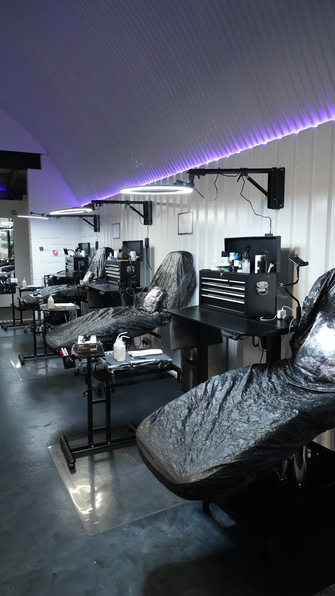 Three tattoo workstations inside London's Glitch — black beds, tool chests and ring lights under the corrugated arch