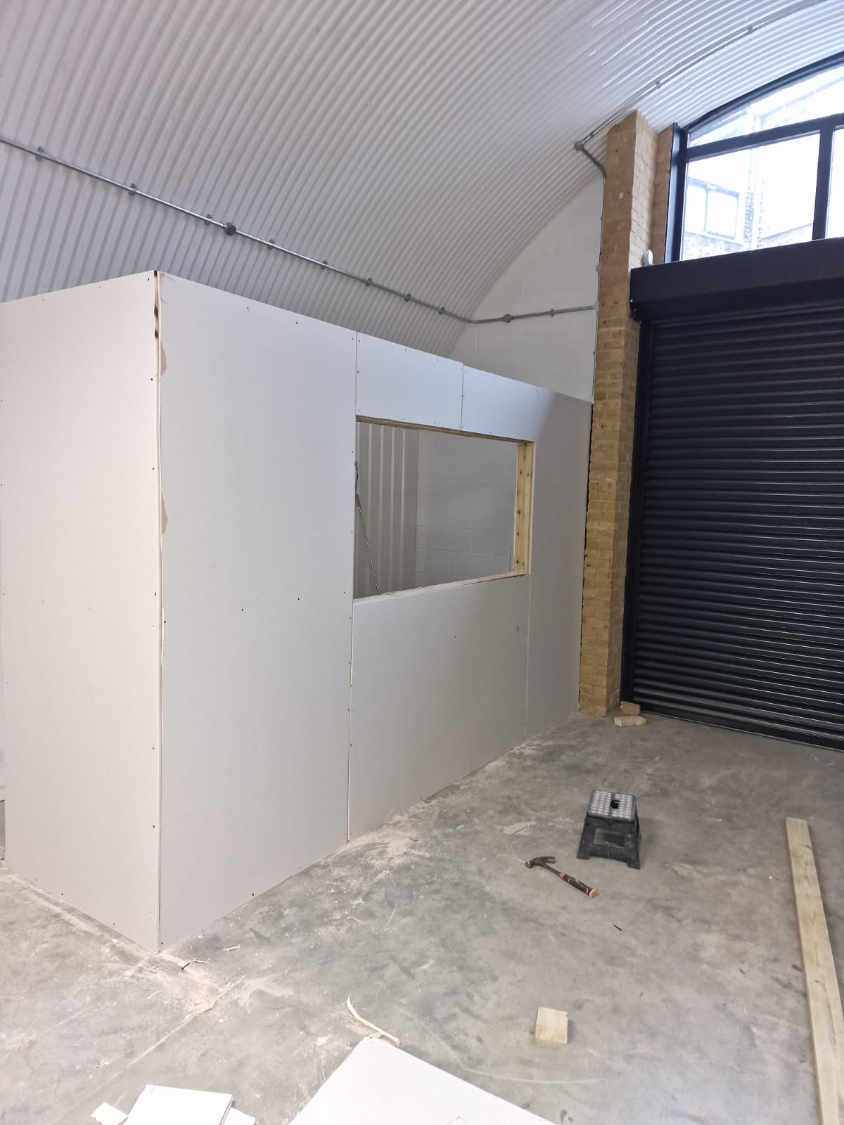 Unfinished plasterboard wall and roller shutter inside the arch at the start of the renovation